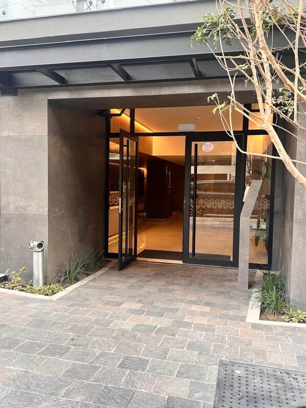 A building entrance with a glass door, a metal staircase, and a small garden area. - Studio with AC, desk, view and pool in Larco (Miraflores)
