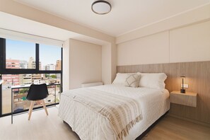 Une chambre moderne avec un grand lit, une table de chevet, un bureau avec une chaise et une vue sur la ville grâce à une grande fenêtre.
