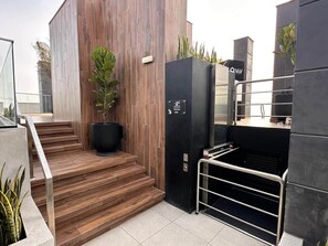 A modern building with a staircase leading to a black elevator, a potted plant, and a metal railing. - 1 bedroom with A/C, desk, coworking space, and pool in Larco (Miraflores)