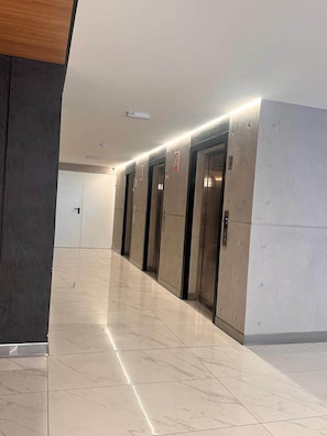 A hallway with a tiled floor, a wooden panel on the left, and three elevators. - Deluxe 1BR · A/C, Pool & Workspace · Miraflores (Miraflores)