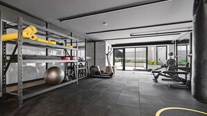 A gym with exercise equipment, a punching bag, and a view through large windows. - Bright Premium AC 1BR · Larco · 24h Reception (Miraflores)