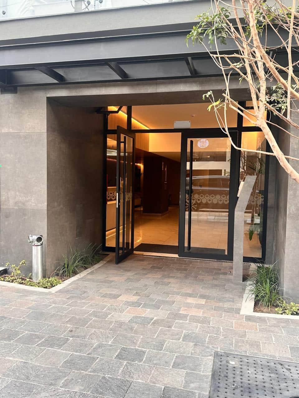 Une entrée d’immeuble avec une porte en verre, un escalier en métal et un petit espace aménagé en jardin.
