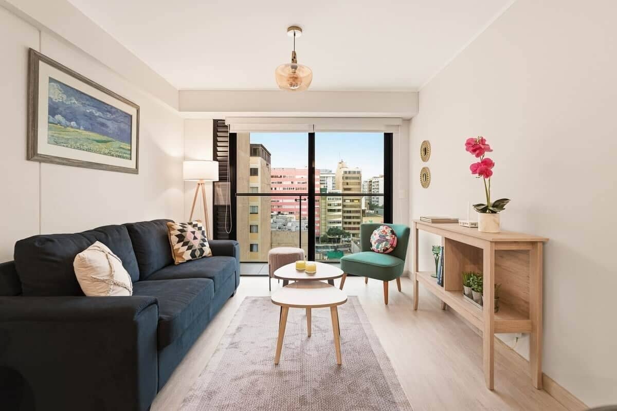 Un salon moderne avec un canapé, une table basse et une vue sur la ville grâce à de grandes fenêtres.