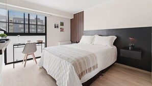 Une chambre à coucher moderne avec un grand lit, un bureau avec une chaise et une fenêtre équipée de stores.