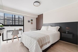 Ein modernes Schlafzimmer mit einem großen Bett, einem Schreibtisch mit Stuhl und einem Fenster mit Jalousien.