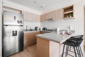 Eine moderne Küche mit einem Edelstahl-Kühlschrank, Holzschränken, einer Granit-Arbeitsplatte und schwarzen Barhocker.