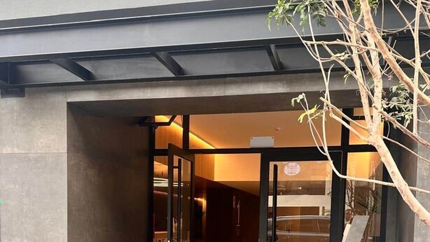 Une entrée d’immeuble avec une porte en verre, un escalier en métal et un petit espace aménagé en jardin.