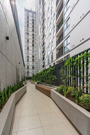 Edifici modern amb una passarel·la central flanquejada per jardineres i vegetació.