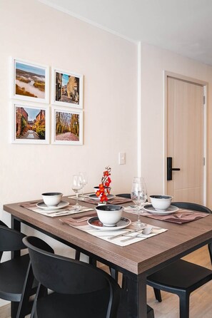 A dining area with a wooden table set for four, chairs, and framed pictures on the wall. - 2BR/2BA for 6 · A/C Bedrooms · Pool · 24/7 Doorman (Miraflores)