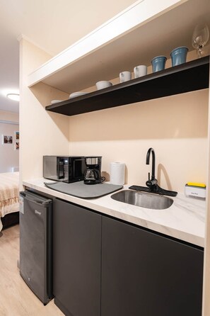 A compact kitchenette with a microwave, coffee maker, and a sink. - Studio + Desk · Split A/C · Pool · 24/7 Doorman (Miraflores)