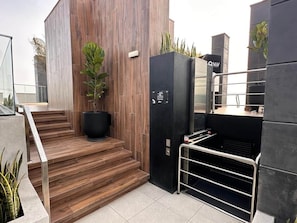 A modern building with a staircase leading to a black elevator, a potted plant, and a metal railing. - Studio with A/C, desk and coworking space in Larco (Miraflores)