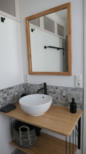 Une salle de bain avec un lavabo sur colonne blanc, un plan de toilette en bois, un miroir et un porte-serviettes.