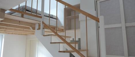Una escalera de madera con una pared blanca y una ventana con mosquitero.