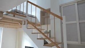 Eine Holztreppe mit einer weißen Wand und einem Fenster mit Insektenschutzgitter.