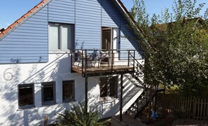 Une maison à deux étages avec un balcon, un escalier en bois et un petit jardin.