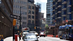 Uma rua urbana com edifícios, um ônibus e veículos.