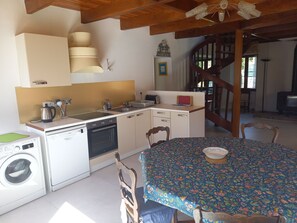 A compact kitchen with a washing machine, a stove, and a dining table with chairs. - Comfortable family home walking distance to the beach (Névez)