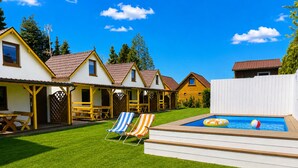 A backyard with a swimming pool, lounge chairs, and a wooden deck. - Cottages for 4 People With a Swimming Pool, Dziwnowek (Kamien Pomorski)
