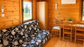 A wooden cabin interior with a sofa, dining table, chairs, and an air conditioning unit. - Cottages for 4 People With a Swimming Pool, Dziwnowek (Kamien Pomorski)