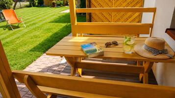 A wooden outdoor table with a book, sunglasses, and a drink on it.