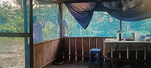 A room with a wooden floor, a blue stool, a table with various items, and a view of greenery outside.