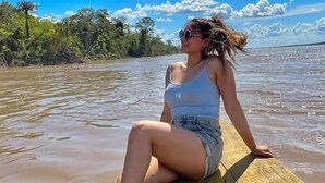 Una persona sentada en un muelle de madera junto a un cuerpo de agua, con árboles al fondo.