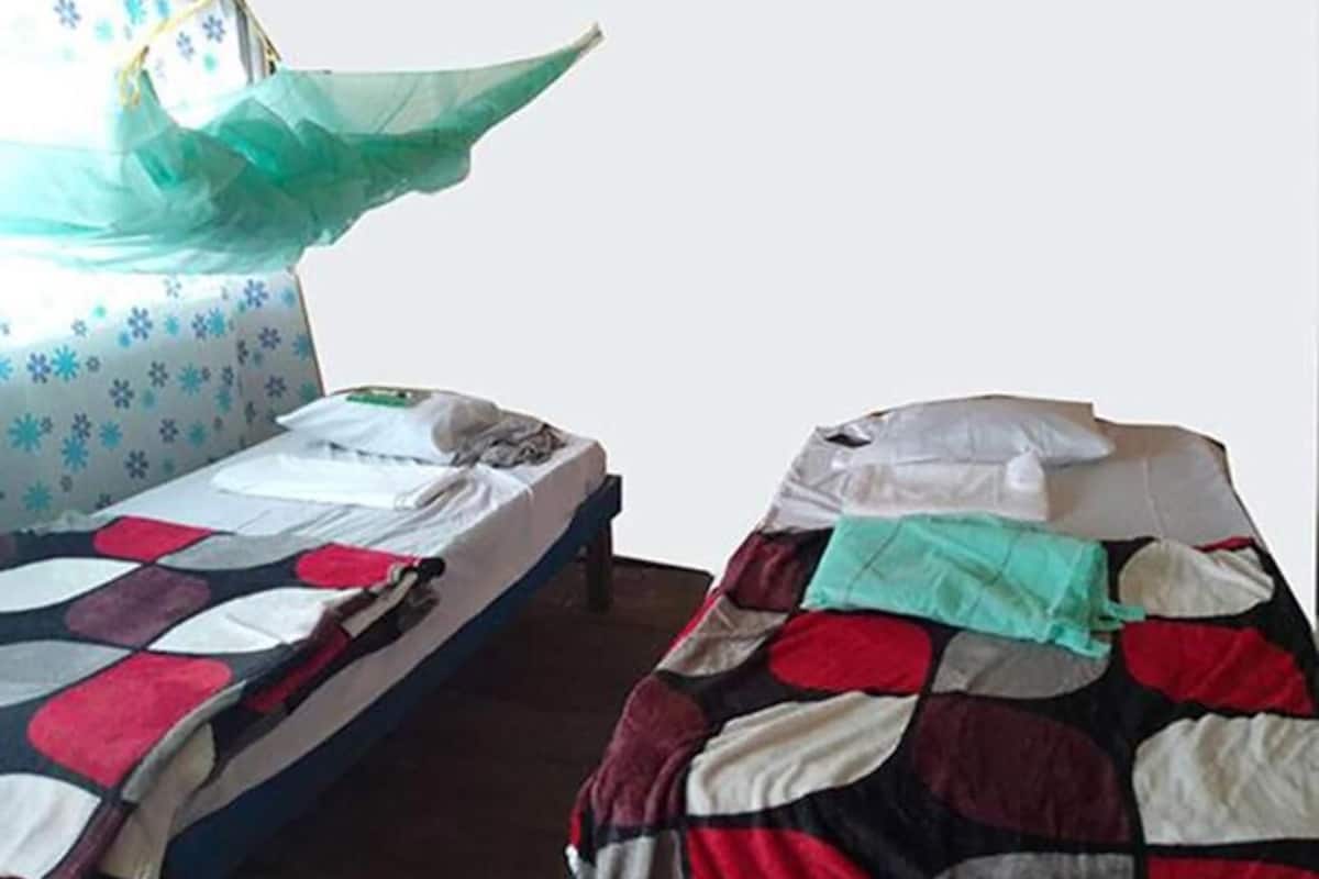 Dos camas individuales con diferentes diseños de ropa de cama, una mosquitera y una ventana con cortina estampada.