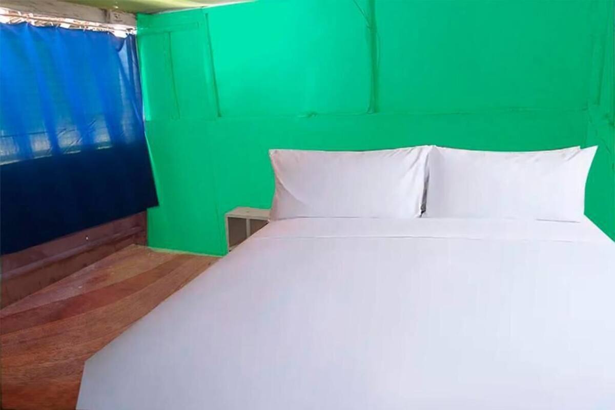 Una habitación con cama, mesita de noche y ventana con cortinas.