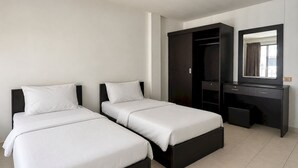 A hotel room with two beds, a dark wooden wardrobe, a desk, and a mirror. - Collection O Central Pattaya Residence (Pattaya)