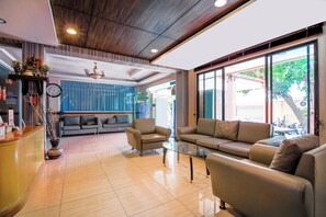 A modern living area with a sofa, armchairs, a glass coffee table, a reception desk, and a clock.