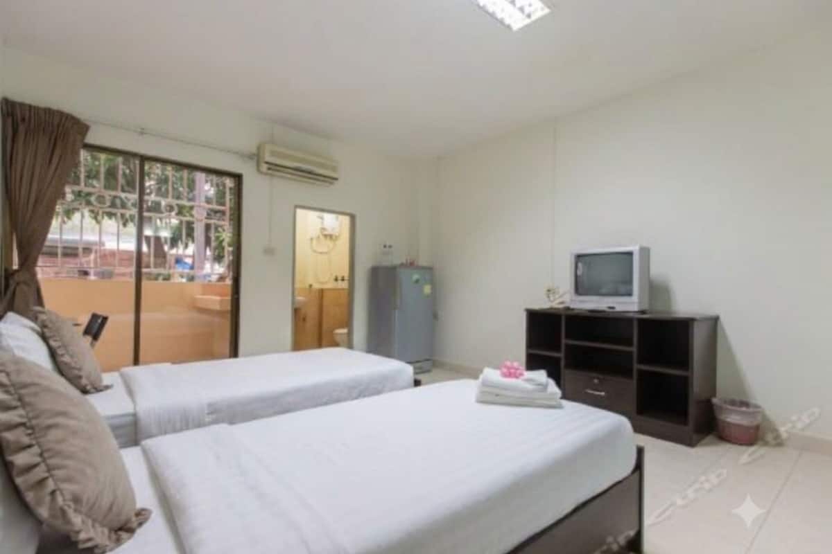 A hotel room with two beds, a television, a wardrobe, and a sliding glass door leading to an outdoor area.