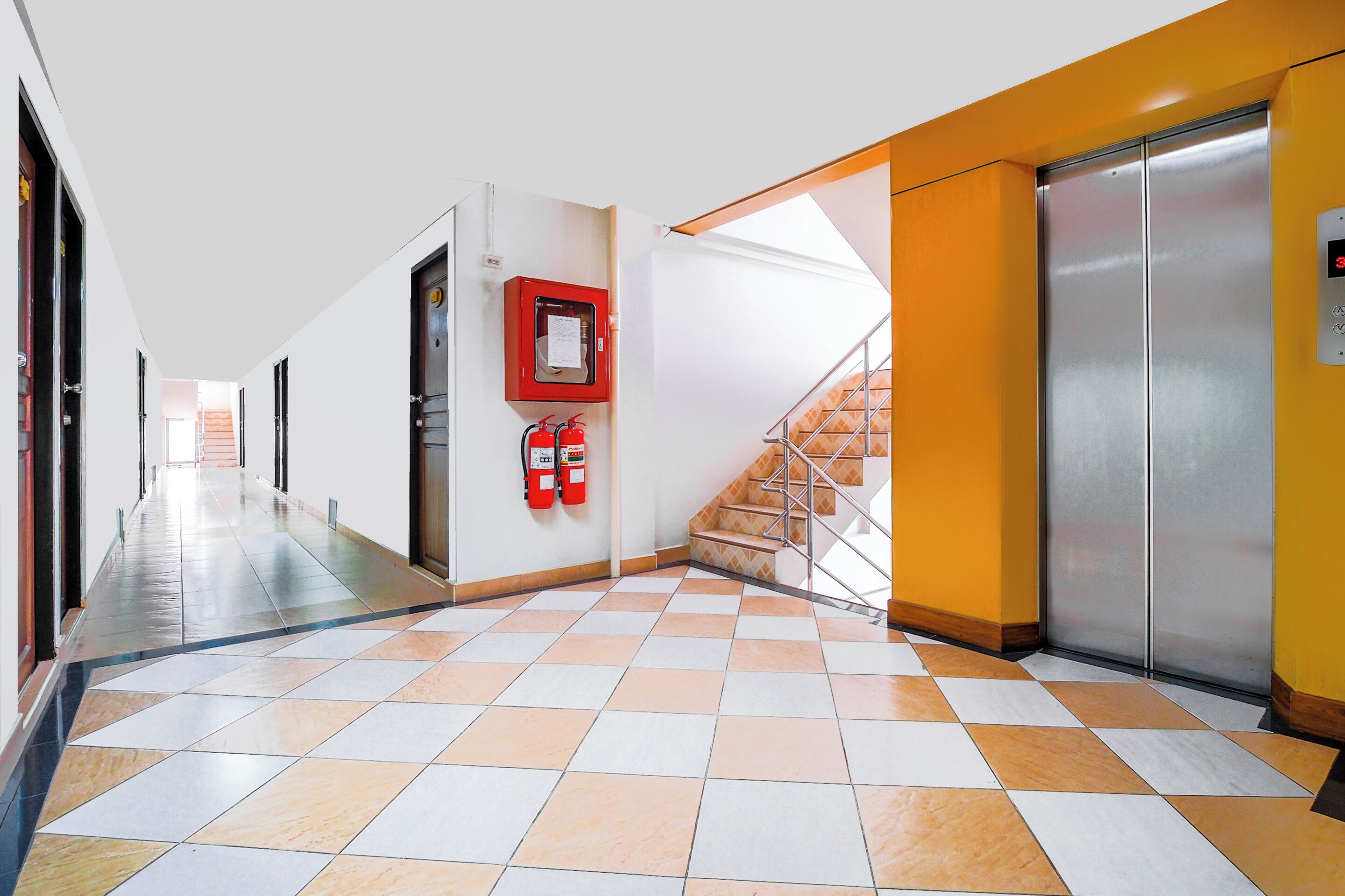 A corridor with a checkered floor, a fire extinguisher, and an elevator.