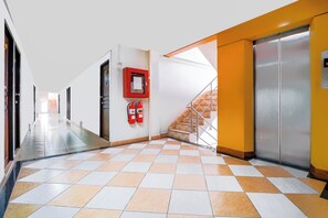 A corridor with a checkered floor, a fire extinguisher, and an elevator.