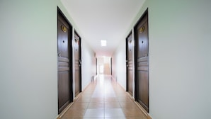 A long, narrow hallway with wooden doors on both sides and a tiled floor. - Collection O Central Pattaya Residence (Pattaya)