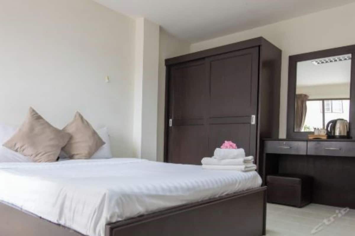 A neatly made bed with pillows, a dark wooden wardrobe, and a mirror above a dresser.
