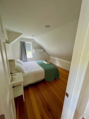Une chambre à coucher avec un lit, une table de chevet, une fenêtre avec des rideaux et un plancher en bois.