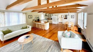 A spacious living area with a sofa, coffee table, and a dining table with chairs. A kitchen is visible in the background.