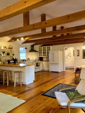 A spacious kitchen with wooden beams, a central island with stools, and a dining area with a chair and table.