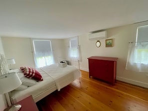 Une chambre à coucher comprenant un lit, une table de chevet, une commode, une fenêtre avec des rideaux et un appareil de climatisation.