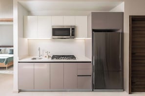 A compact kitchen with a built-in microwave, a stainless steel refrigerator, and a gas stove. - BlueMall Luxury Suites by Homeclub (Santo Domingo)