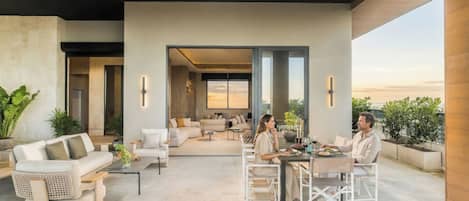 Un espacio exterior moderno con comedor, sofás y vista al atardecer.
