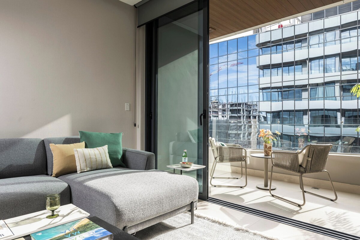 A modern living room with a sofa, a small table, and a balcony with chairs.