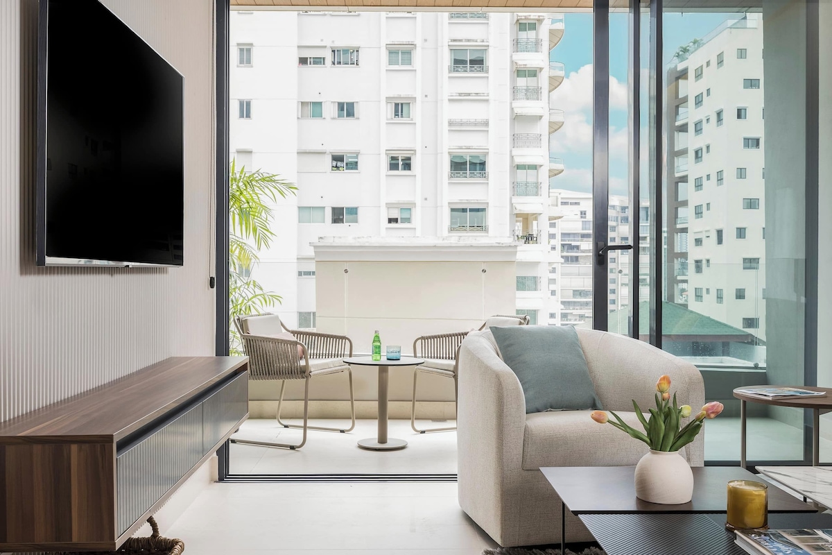 A modern living room with a flat-screen TV, a sofa, a coffee table, and a view of a residential building.