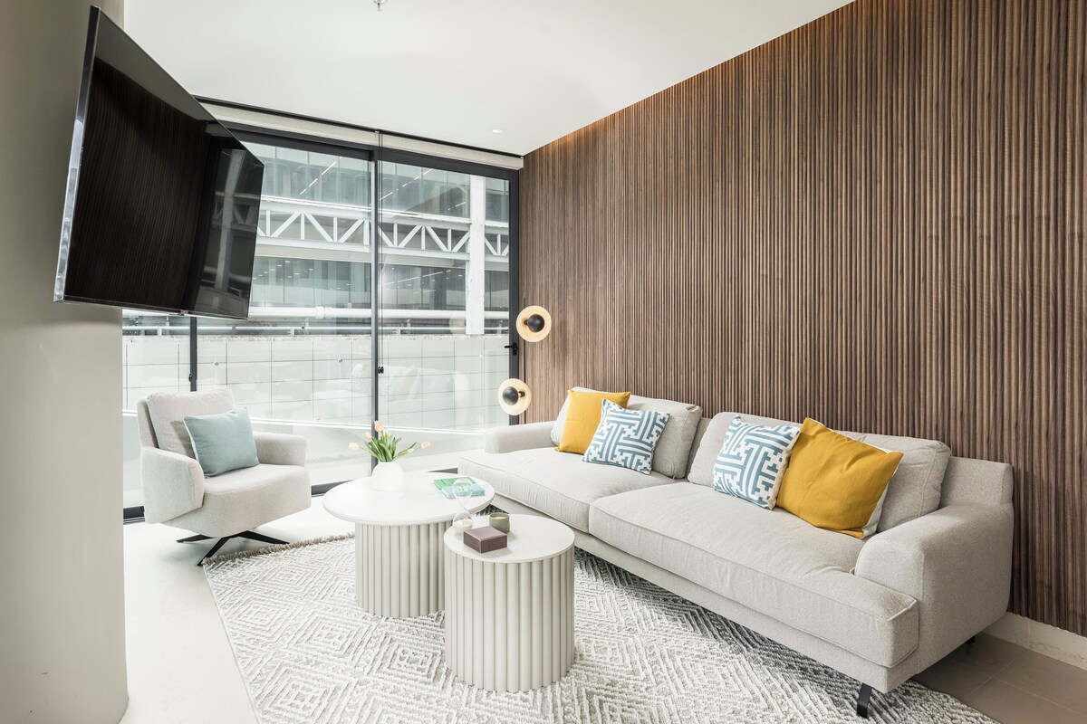 A modern living room with a sofa, armchairs, a coffee table, and a TV mounted on the wall.