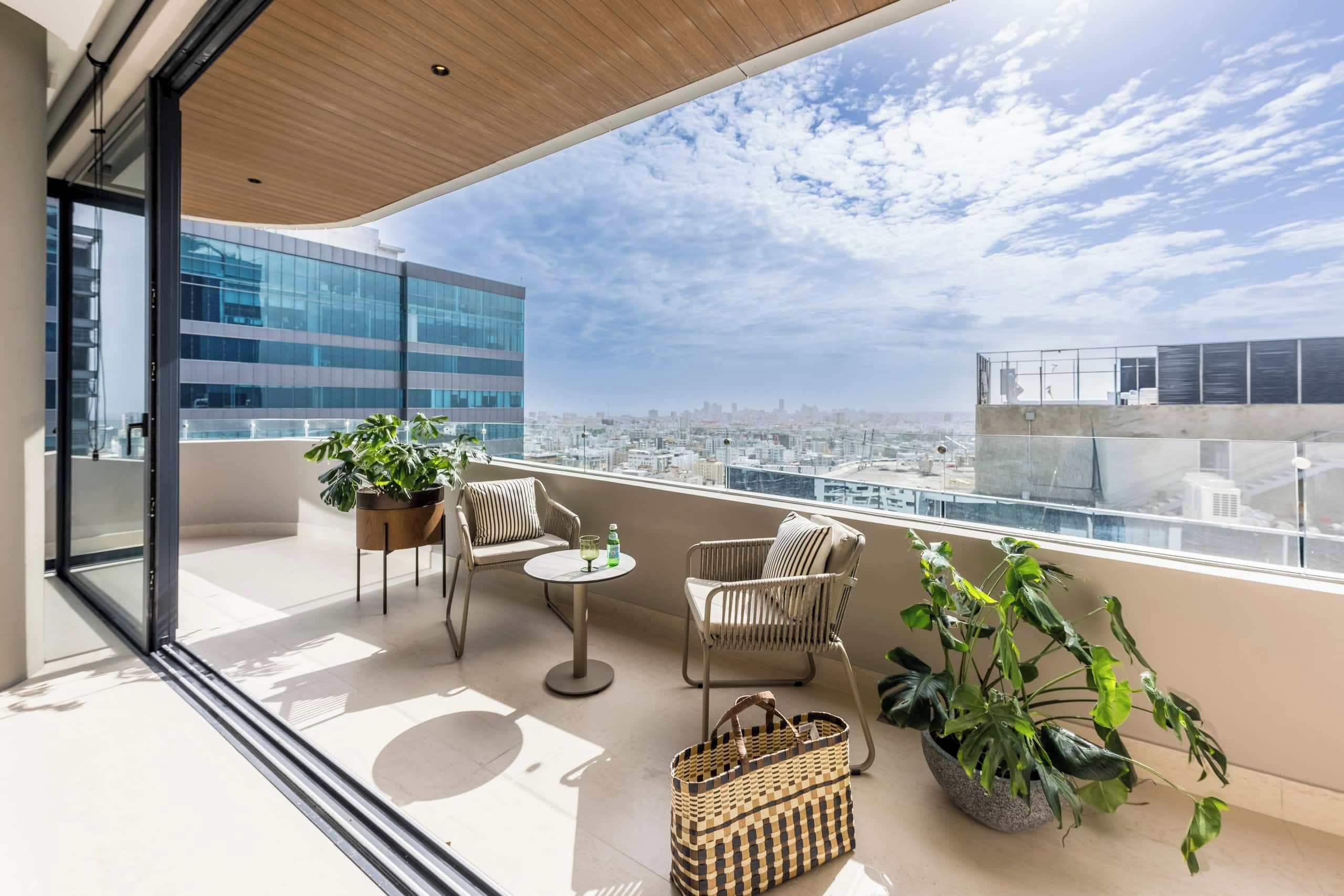 Een balkon met uitzicht op een stadsgezicht, ingericht met twee stoelen, een tafel en plantenpotten.
