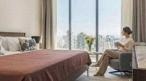A modern hotel room with a large bed, a sitting area, and a view of the cityscape. - BlueMall Luxury Suites by Homeclub (Santo Domingo)