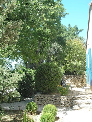 A stone wall, a small garden with a bench, and a tree. - Le clos des lavandes (Lacoste (Provence))