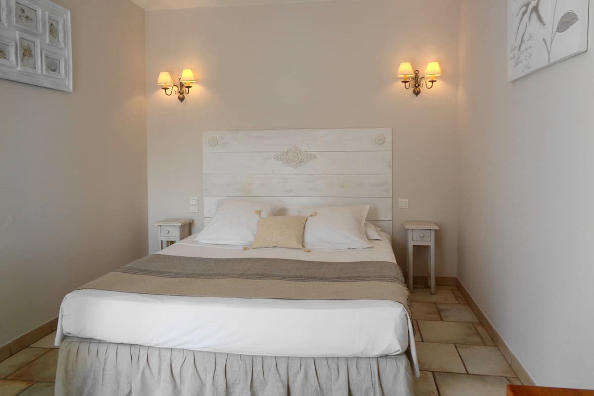 A bedroom with a wooden headboard, two bedside tables, a bed with white and beige bedding, and wall-mounted light fixtures.