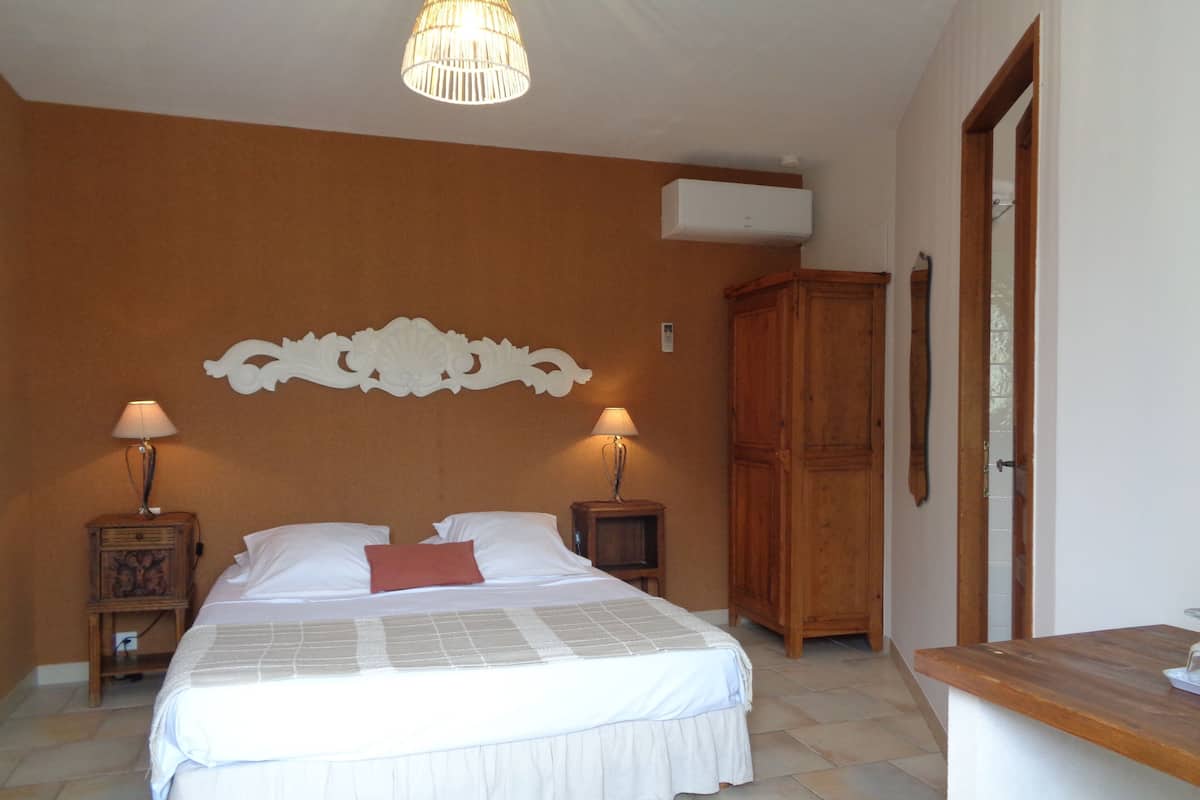 A bedroom with a bed, two bedside tables with lamps, a wooden wardrobe, and a ceiling light fixture.