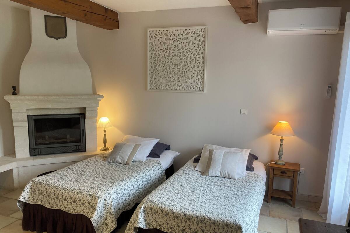 A room with two beds, a fireplace, a wall-mounted air conditioner, and a decorative panel.